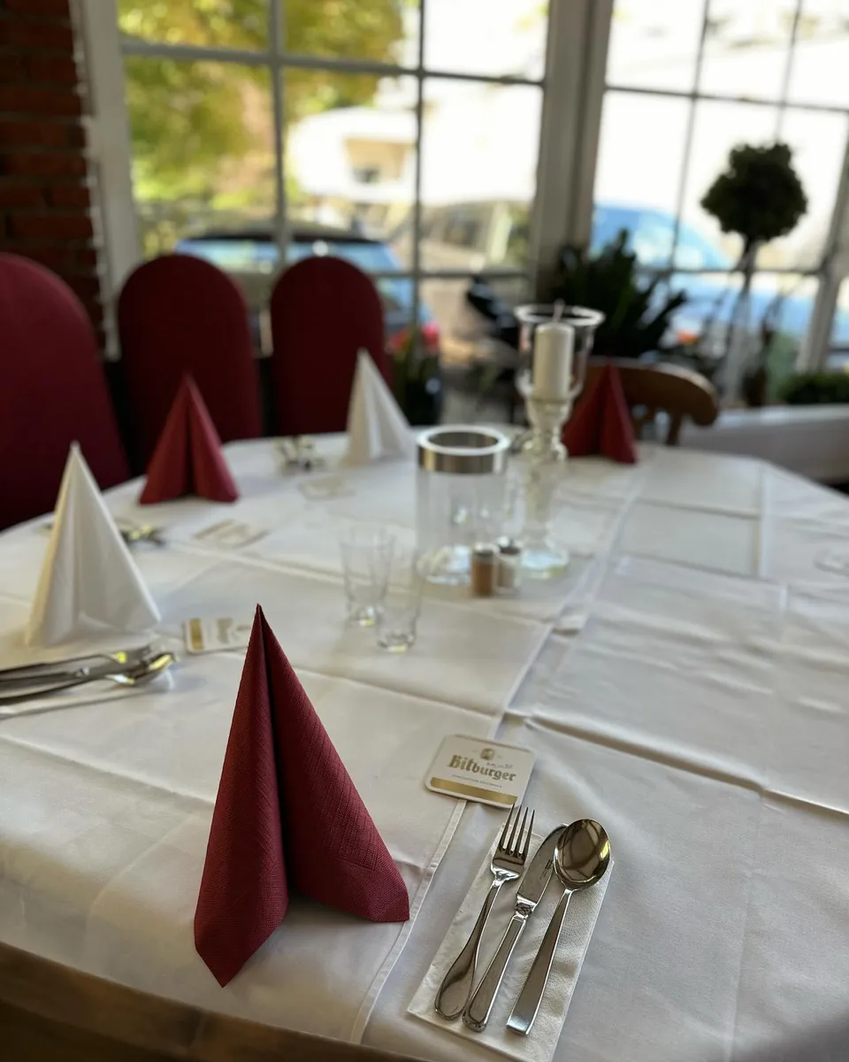 Eingedeckter Tisch mit weißer und bordeauxroter Serviette am Fenster