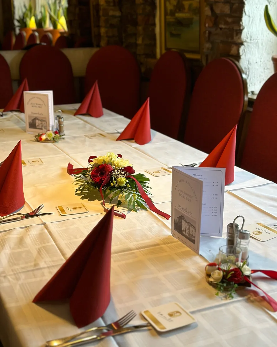 Gedeckte Tafel mit roten Servietten, Blumengesteck und Menükarte